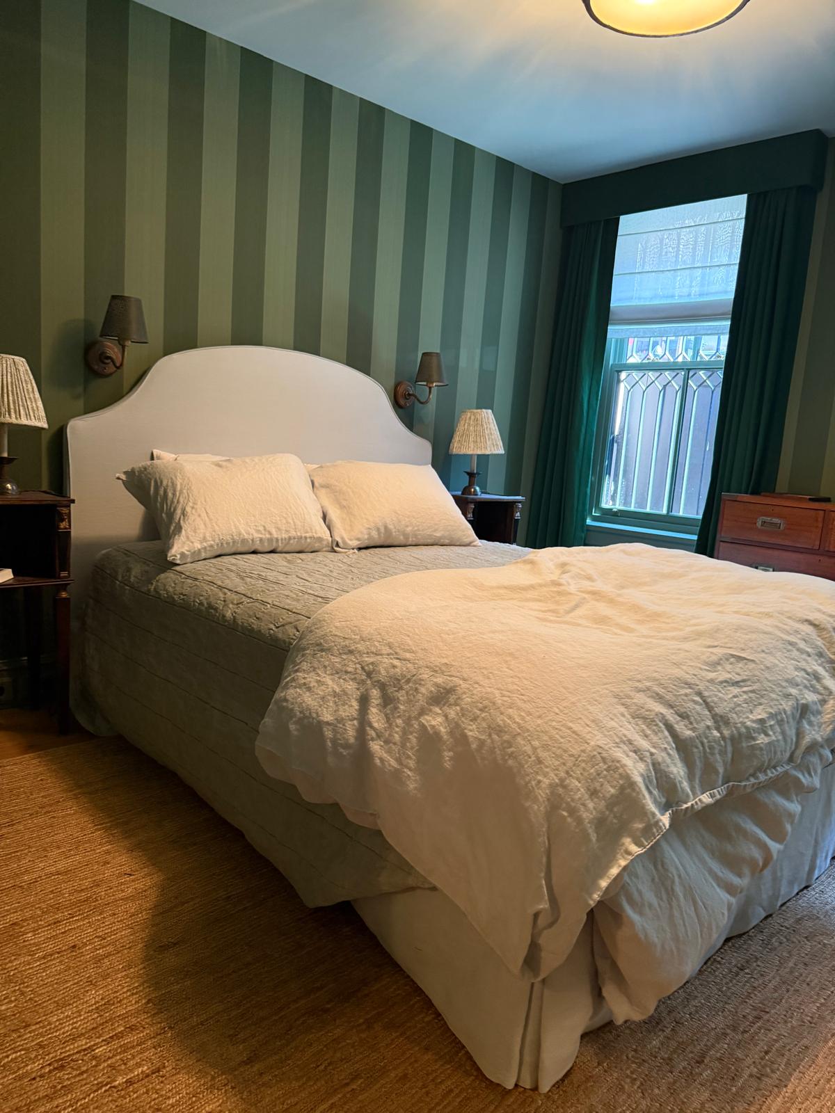 White arched upholstered headboard in green striped bedroom