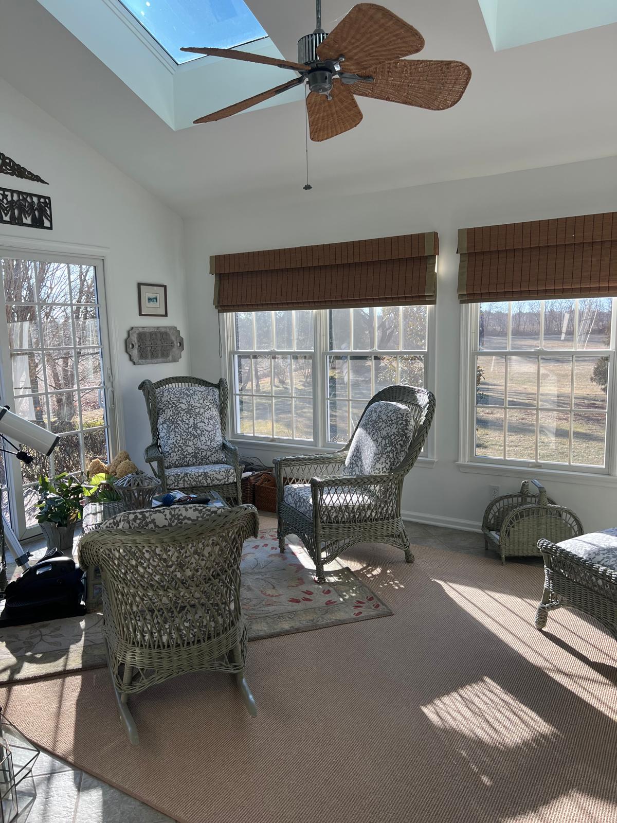 Wicker chairs with upholstered cushions and bamboo roman shades in sunroom